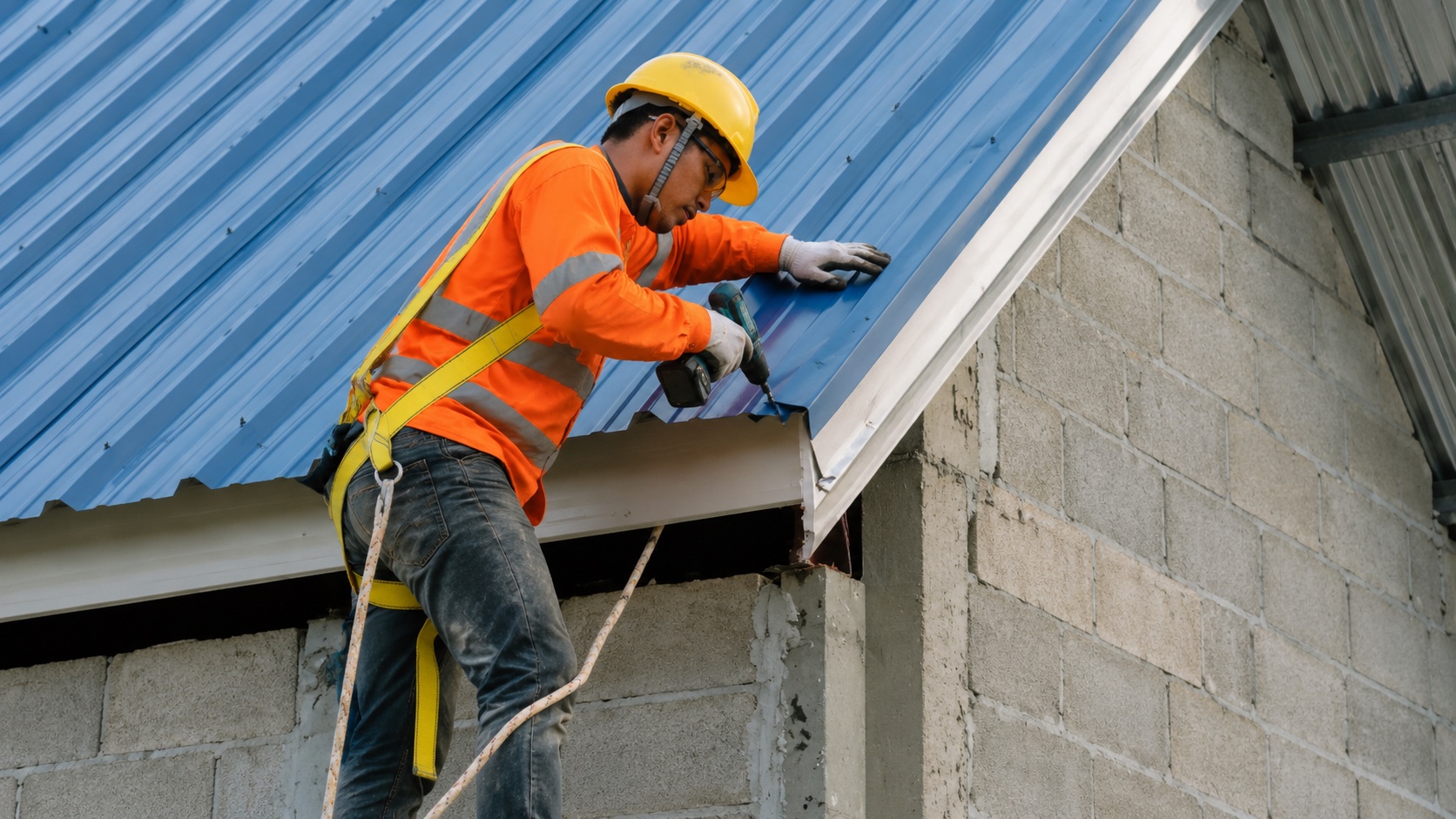 Roofer installing a blue metal roofing panel