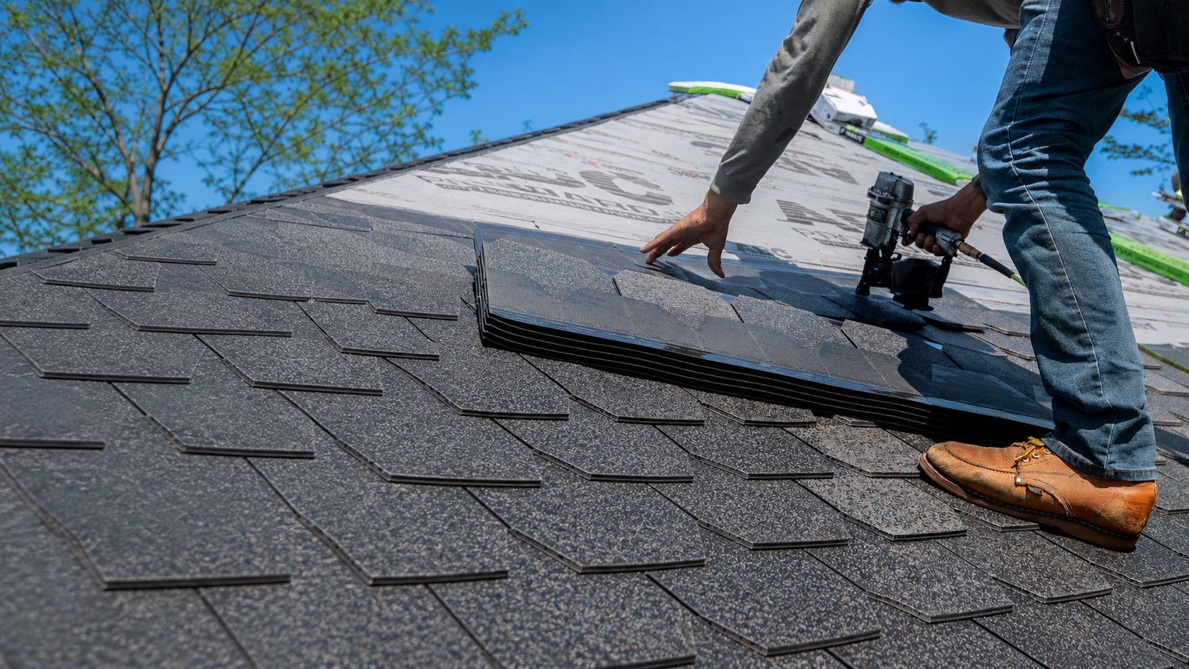 Residential roofer installing asphalt shingles with a nail gun